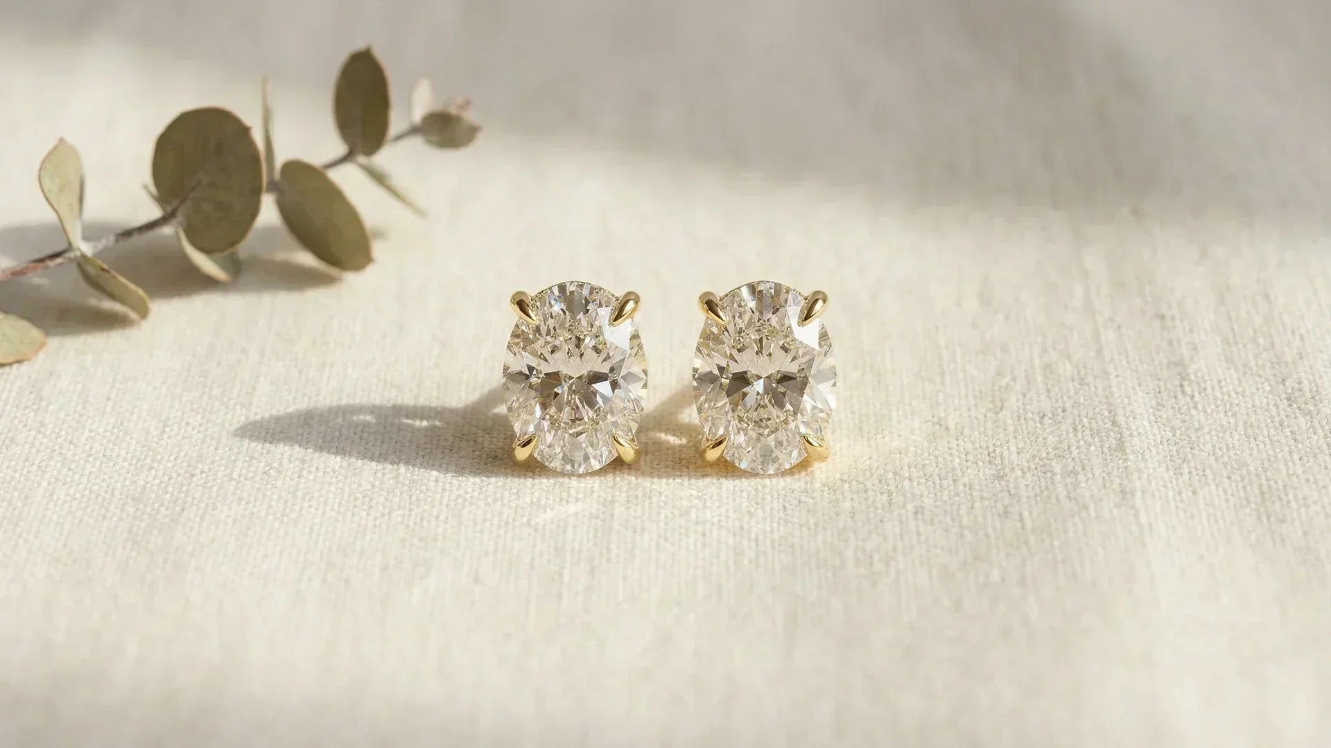 Oval hidden halo lab-grown diamond earrings on linen surface 