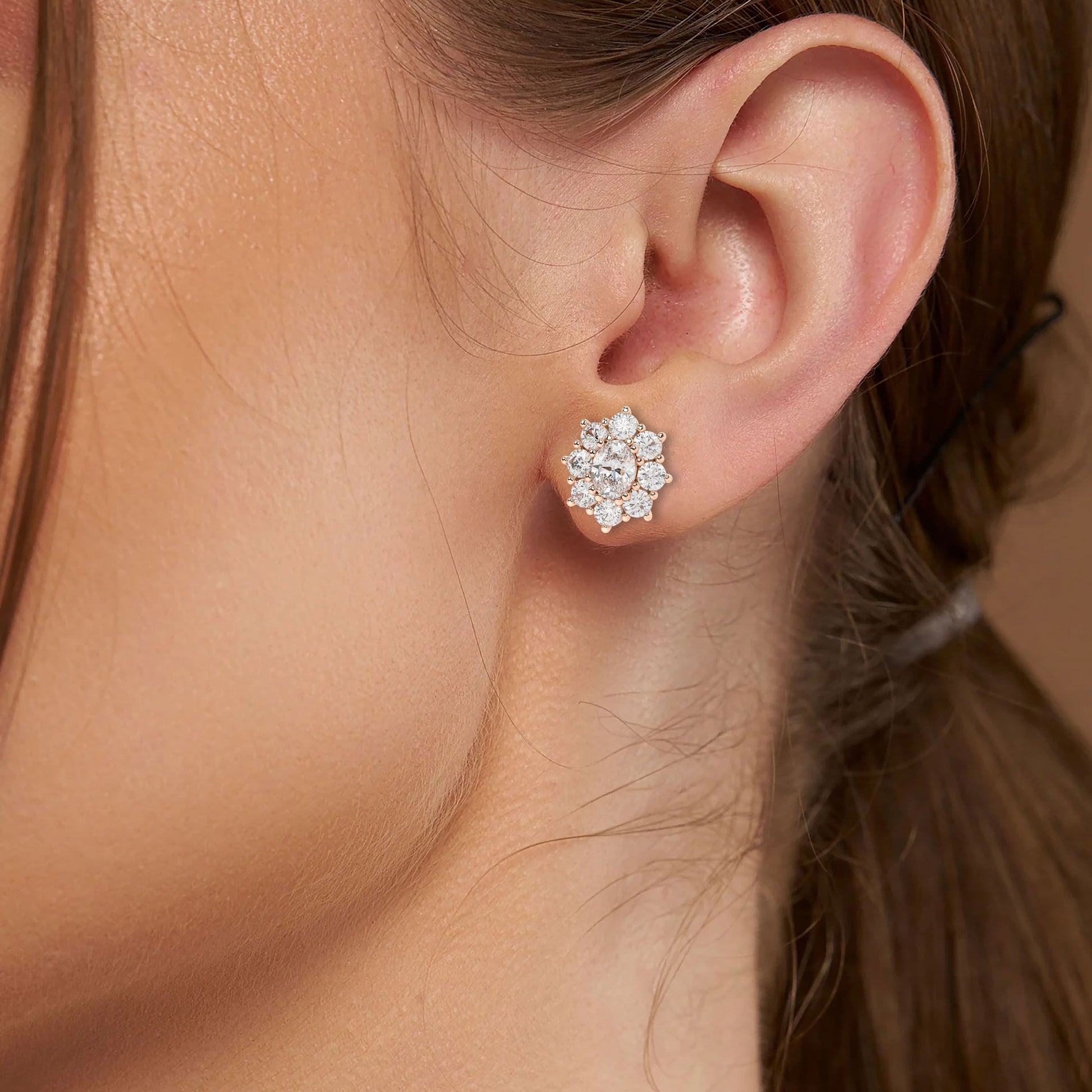 Model wearing rose gold lab-grown diamond halo stud earrings with oval centerpiece and dazzling round diamond halo, ear side view, feminine diamond pieces