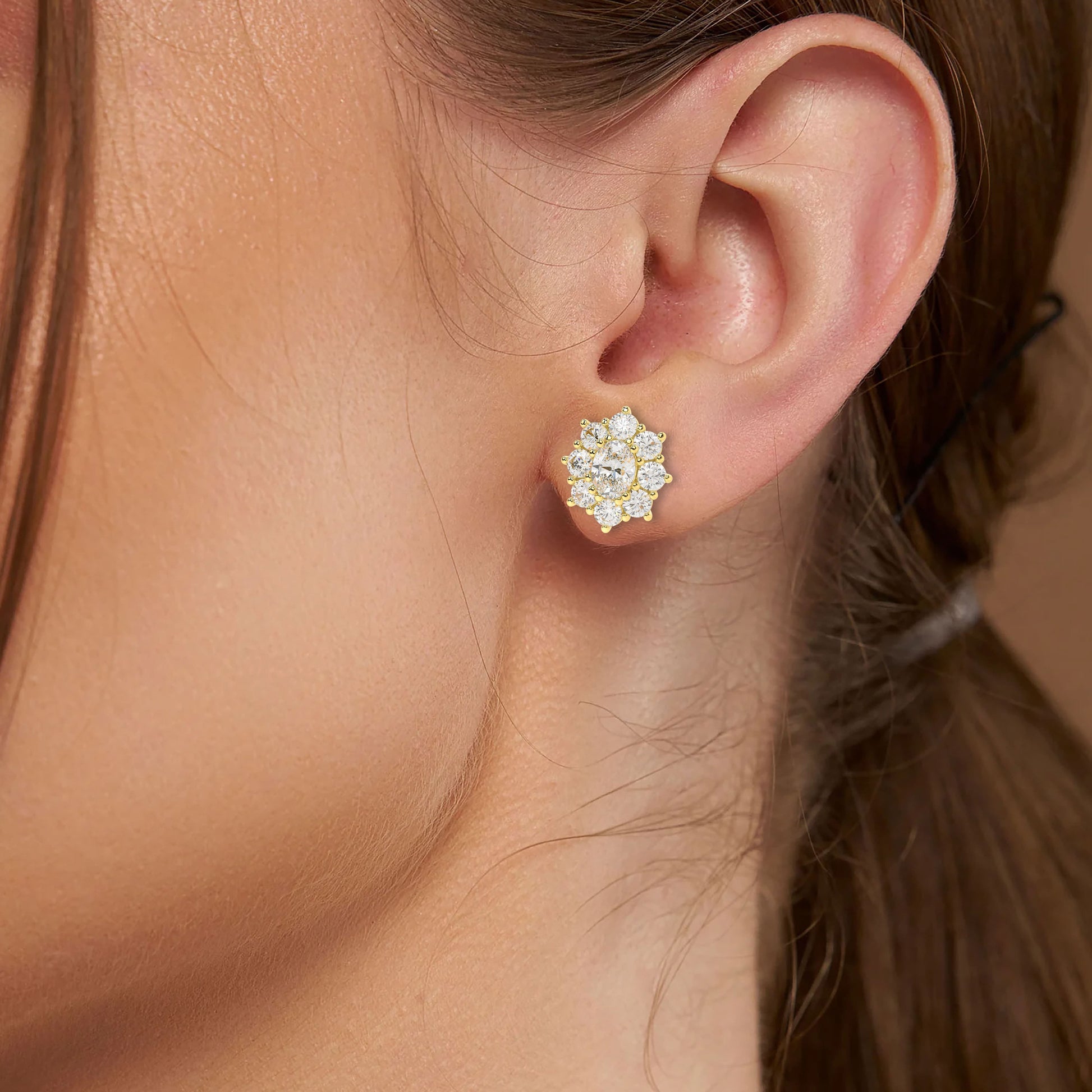 Model wearing yellow gold lab-grown diamond halo stud earrings featuring oval center stone and sparkling round diamond cluster, side profile view, elegant diamond jewelry
