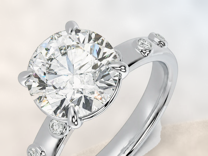 Round diamond solitaire with spaced round bezel accents along the band