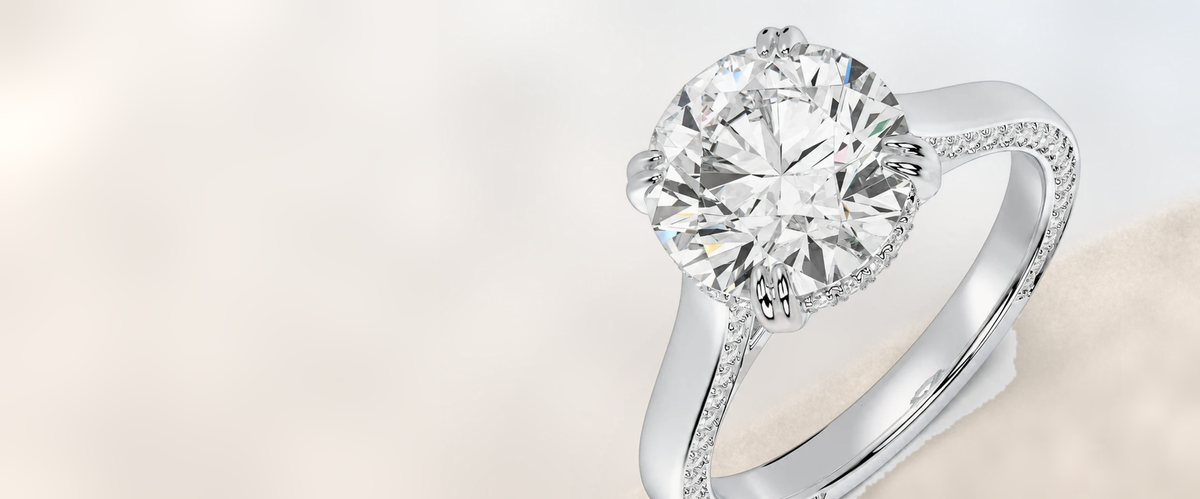 Round lab-grown diamond solitaire with paired prongs and a pavé band, resting on sand
